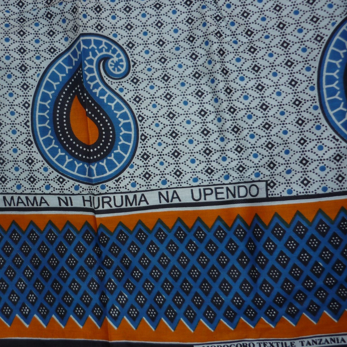Das Foto zeigt einen weiß-blau-organge-gemusterten Kanga, ein Tuch, das in Ostafrika ein typisches Kleidungsstück ist.